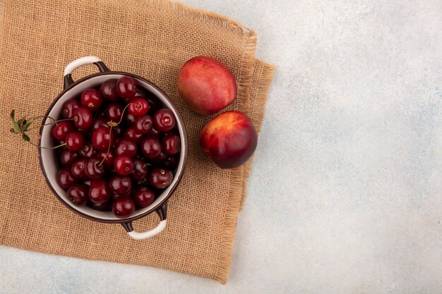 Bovenaanzicht van fruit als kersen in kom en perziken op zak en witte achtergrond met kopie ruimte