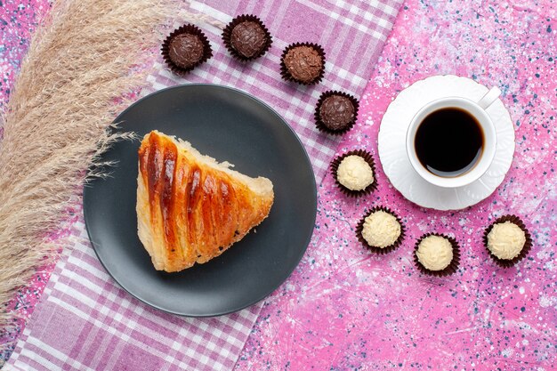 Bovenaanzicht van gebakjesplak met kopje thee en chocoladesuikergoed op roze oppervlak
