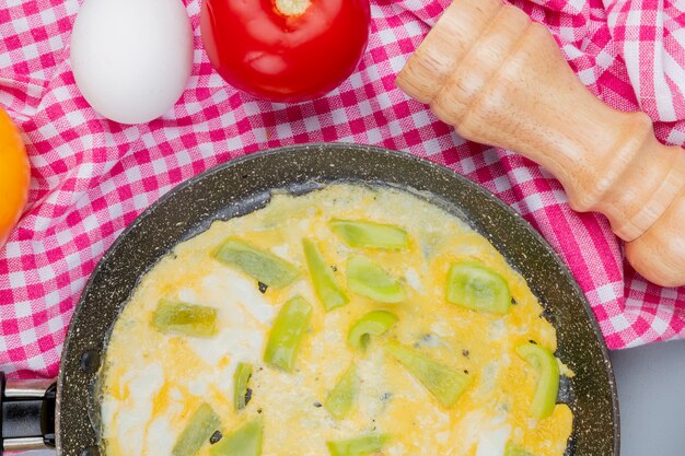 Bovenaanzicht van gebakken eieren op een koekenpan met groene paprika segmenten op een gecontroleerde doek op een witte achtergrond