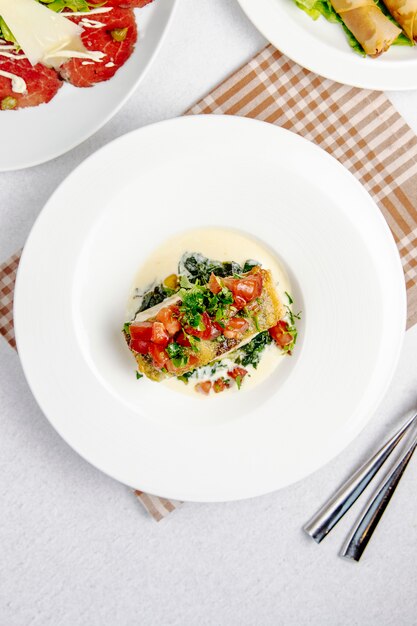 Bovenaanzicht van gebakken zeebaars met tomaten op witte plaat