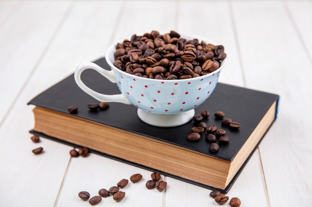 Bovenaanzicht van gebrande koffiebonen op een polka dot cup op een witte houten achtergrond
