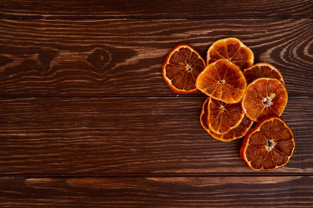 Bovenaanzicht van gedroogde stukjes sinaasappel gerangschikt op houten achtergrond met kopie ruimte