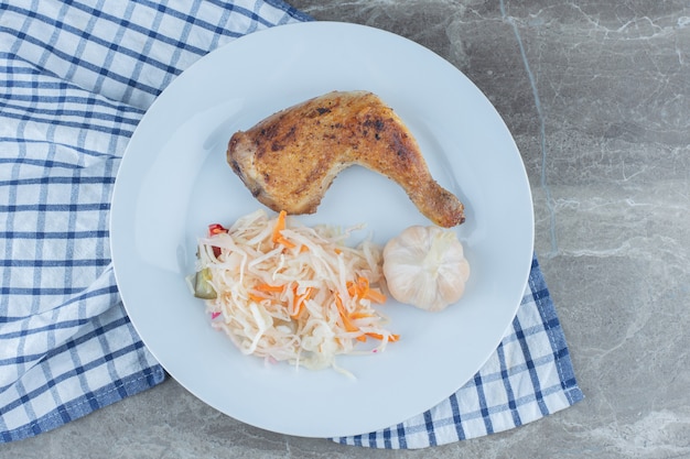 Bovenaanzicht van gegrilde kip en zuurkool op witte plaat.