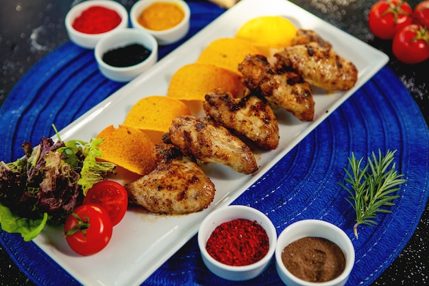 Bovenaanzicht van gegrilde kippenvleugeltjes geserveerd met gebakken aardappelen en verse salade