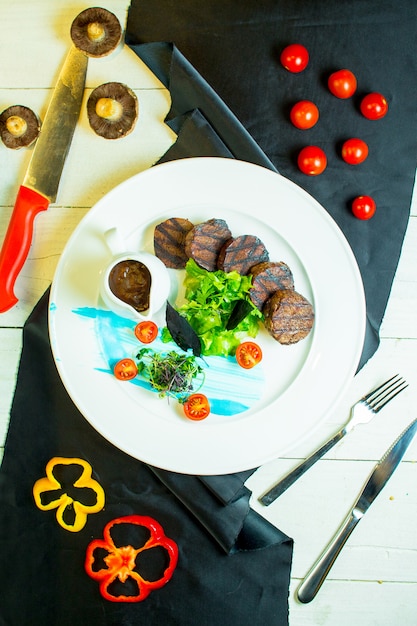 Bovenaanzicht van gegrilde medaillons van rundvlees met cherrytomaatjes en saus op een plaat