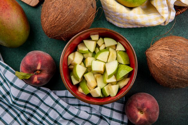 Bovenaanzicht van gehakte appelschijfjes op rode kom met kokos perziken op chekcked en groen