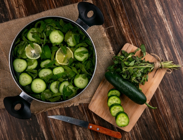 Bovenaanzicht van gehakte komkommers met munt in een pan met een snijplank en mes op een houten oppervlak
