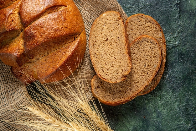 Bovenaanzicht van geheel en gesneden dieet zwart brood en spikes op bruine handdoek op donkere kleuren oppervlak