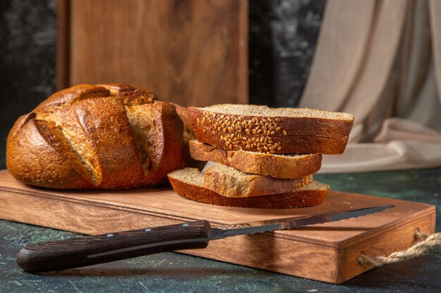 Bovenaanzicht van geheel en gesneden zwart brood op bruine houten snijplank op donkere ondergrond