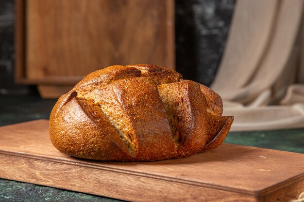 Bovenaanzicht van geheel zwart brood op bruine houten snijplank op donkere kleuren oppervlak