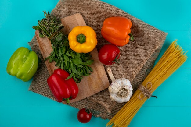 Bovenaanzicht van gekleurde paprika op een snijplank met rauwe spaghetti van munt en knoflook op een turkoois oppervlak