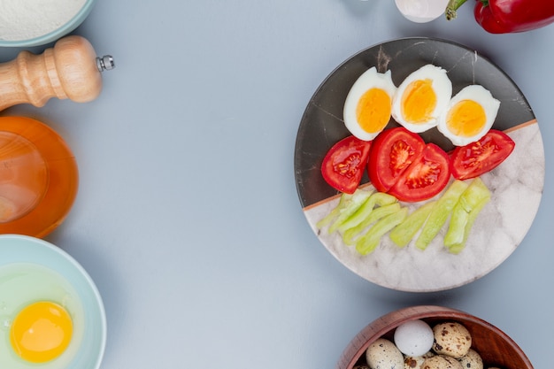 Bovenaanzicht van gekookt ei op een plaat met plakjes tomaten met kwarteleitjes op een houten kom op een witte achtergrond met kopie ruimte