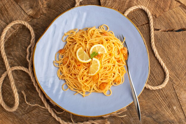 Gratis foto bovenaanzicht van gekookte italiaanse pasta met groenen en schijfjes citroen in blauw bord met touwen op het houten oppervlak