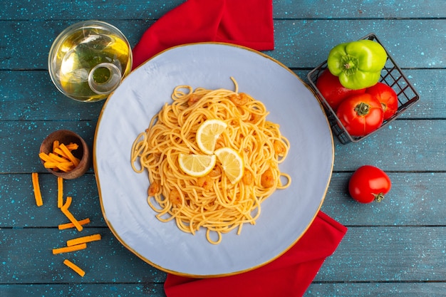 Bovenaanzicht van gekookte italiaanse pasta met plakjes citroen in blauw bord met olie en groenten