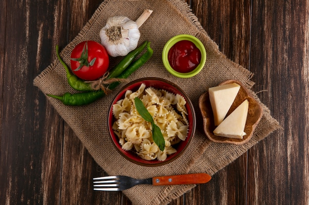 Bovenaanzicht van gekookte pasta in een kom met een vork tomaten chilipepers knoflook en kaas op een beige servet