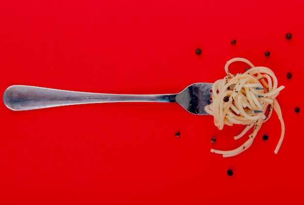 Gratis foto bovenaanzicht van gekookte spaghetti macaroni op vork met zwarte peper zaden op rode ondergrond