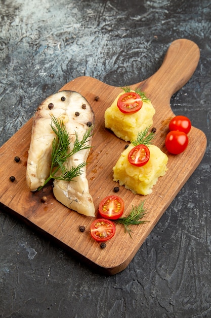 Bovenaanzicht van gekookte vis-boekweitmaaltijd geserveerd met tomaten, groene kaas op houten snijplank op ijsoppervlak
