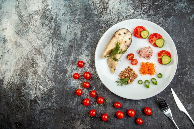 Bovenaanzicht van gekookte visboekweit geserveerd met groenten groen op een wit bord en bestek op ijsoppervlak met vrije ruimte
