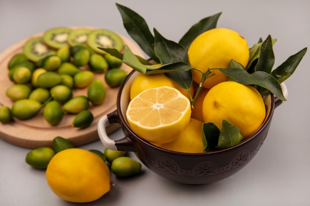 Bovenaanzicht van gele citroenen op een kom met kinkans en kiwiplakken op een houten keukenbord op een witte muur