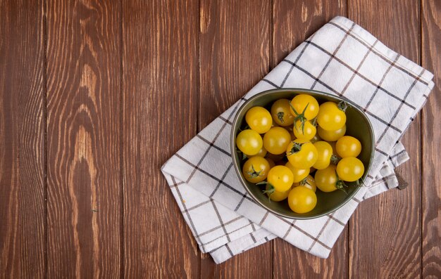 Bovenaanzicht van gele tomaten in kom op doek aan rechterkant en houten tafel