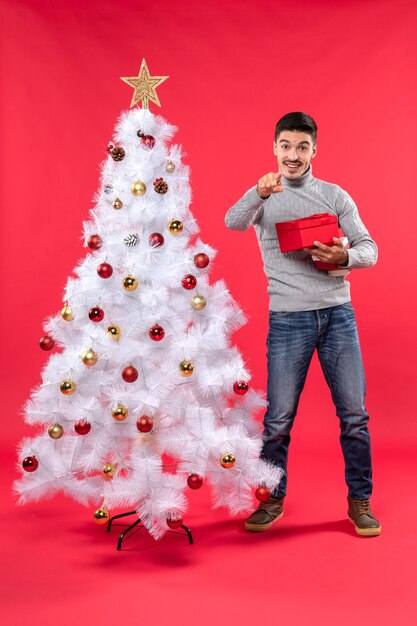 Bovenaanzicht van gelukkig knappe volwassene in een grijze blouse staande in de buurt van de versierde witte kerstboom