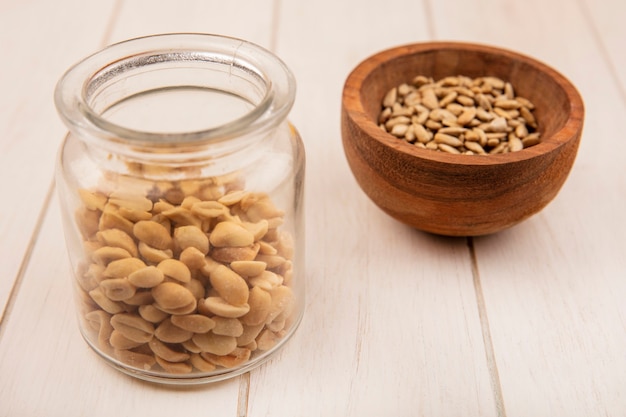 Bovenaanzicht van gepelde zonnebloempitten op een houten kom met pijnboompitten op een glazen pot op een beige houten tafel