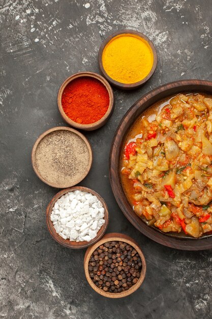 Bovenaanzicht van geroosterde auberginesalade in kom en verschillende kruiden op donkere ondergrond