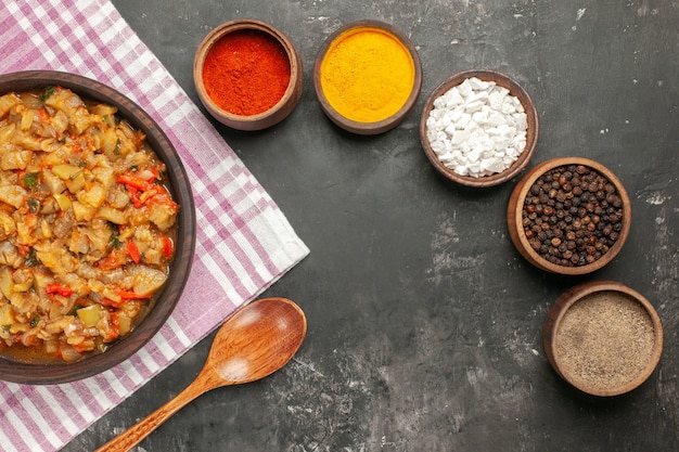 Bovenaanzicht van geroosterde auberginesalade in kom houten lepel verschillende kruiden in kommen op donkere ondergrond