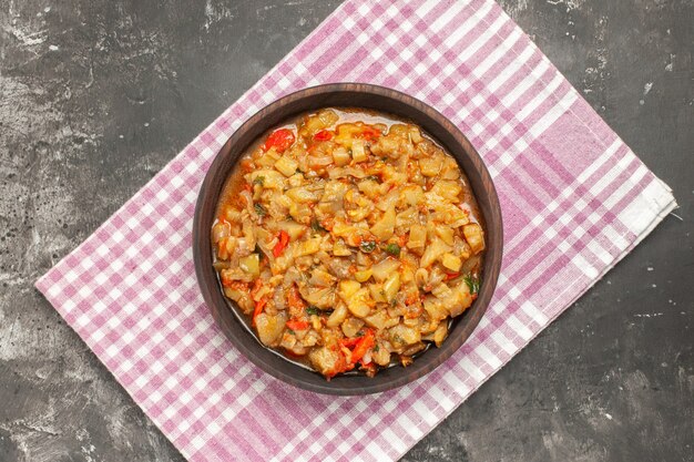 Bovenaanzicht van geroosterde auberginesalade in kom op roze wit checered servet op donkere ondergrond