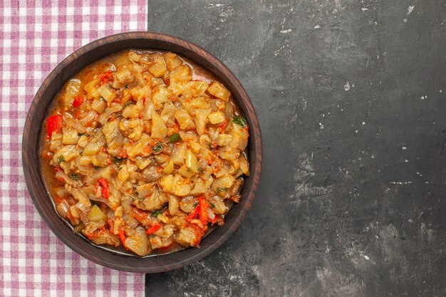 Bovenaanzicht van geroosterde auberginesalade in kom op roze wit geruit oppervlak