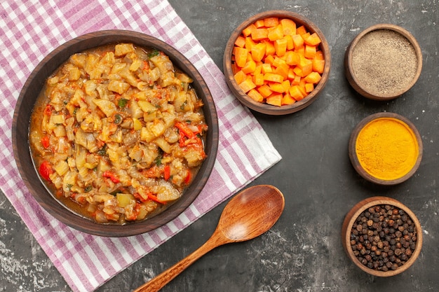 Bovenaanzicht van geroosterde auberginesalade in komkommen met verschillende kruiden snijdt welpen van wortel op donkere ondergrond