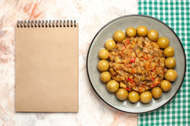 Bovenaanzicht van geroosterde auberginesalade op plaat een notitieblok op naakt oppervlak