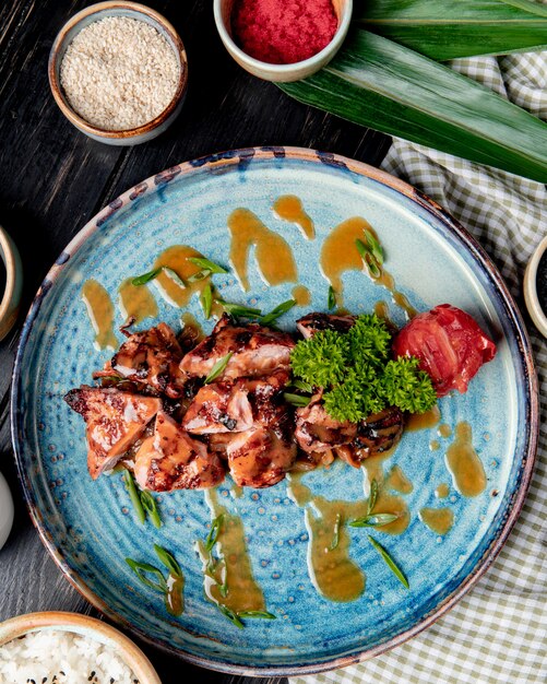 Bovenaanzicht van geroosterde kip met gegrilde tomaten verse kruiden en saus op een plaat op hout