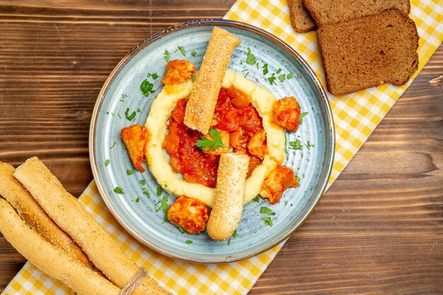 Bovenaanzicht van gesauteerd vlees met aardappelpuree en broden op bruin houten tafel