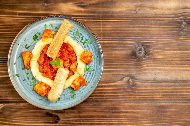 Bovenaanzicht van gesauteerd vlees met aardappelpuree en gesneden broodje op bruin houten tafel. vlees brood aardappel eten