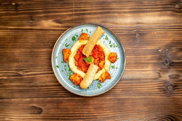 Bovenaanzicht van gesauteerd vlees met aardappelpuree en gesneden broodje op bruin houten tafel