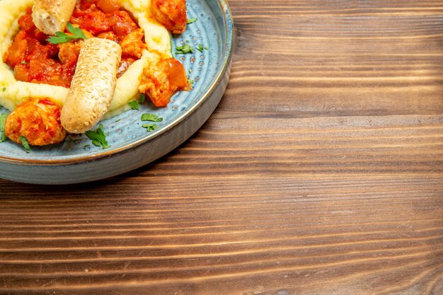 Bovenaanzicht van gesauteerd vlees met aardappelpuree en gesneden broodje op bruin houten tafel