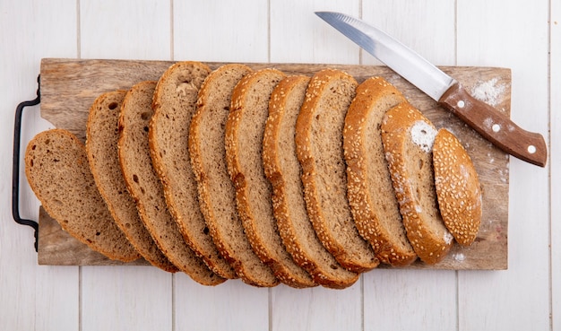 Bovenaanzicht van gesneden bruin gezaaide kolf en mes op snijplank op houten achtergrond