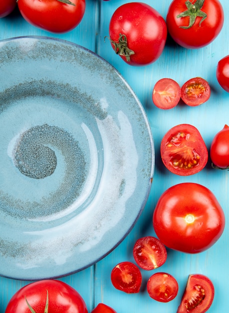 Bovenaanzicht van gesneden en hele tomaten rond plaat op blauw