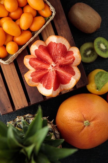 Bovenaanzicht van gesneden grapefruit met kumquats sinaasappel-ananas-kiwi-citroen rond op zwarte achtergrond