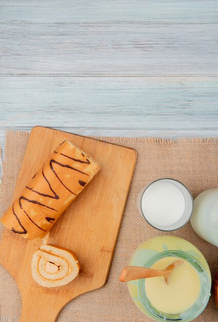 bovenaanzicht van gesneden roll and roll segment op snijplank met melk gecondenseerde melk op zak op houten tafel met kopie ruimte