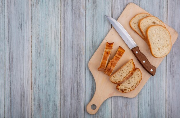 Bovenaanzicht van gesneden stokbrood en mes op snijplank op houten achtergrond met kopie ruimte