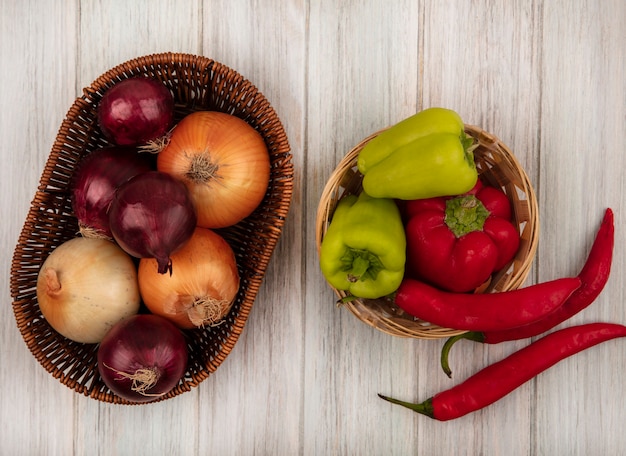 Bovenaanzicht van gezonde en verse uien op een emmer met bel en chilipepers op een emmer op een grijze houten achtergrond