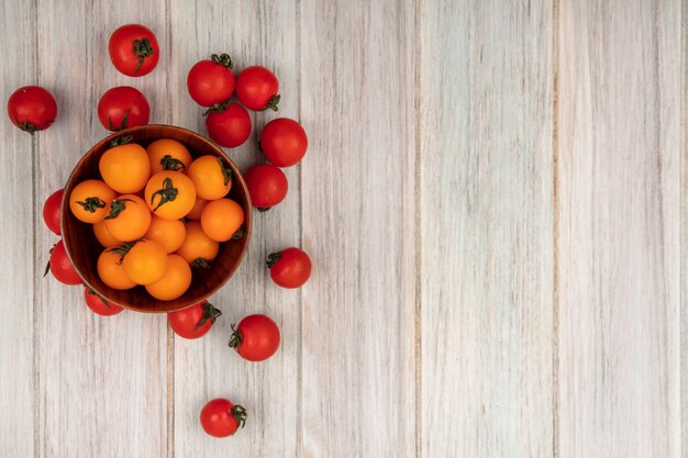Bovenaanzicht van gezonde oranje tomaten op een houten kom met rode tomaten geïsoleerd op een grijze houten oppervlak met kopie ruimte