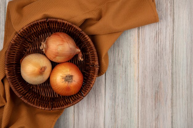 Bovenaanzicht van gezonde uien op een emmer op een doek op een grijze houten muur met kopie ruimte