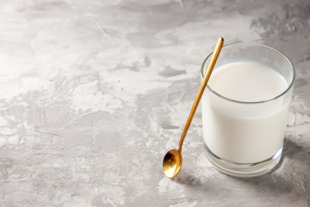 Gratis foto bovenaanzicht van glazen beker gevuld met melk en gouden lepel op grijze tafel met vrije ruimte