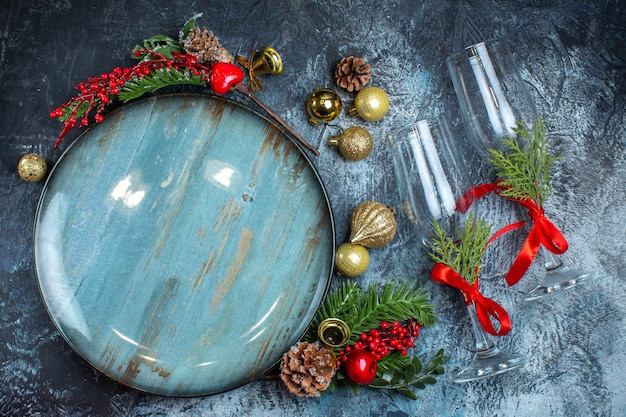 Bovenaanzicht van glazen bekers met rood lint, een blauw bord en decoratieaccessoires van dennentakken op een donkere achtergrond