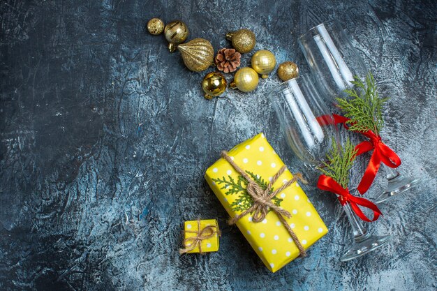 Bovenaanzicht van glazen bekers met rood lint en decoratieaccessoires naast gele geschenkdozen op donkere tafel