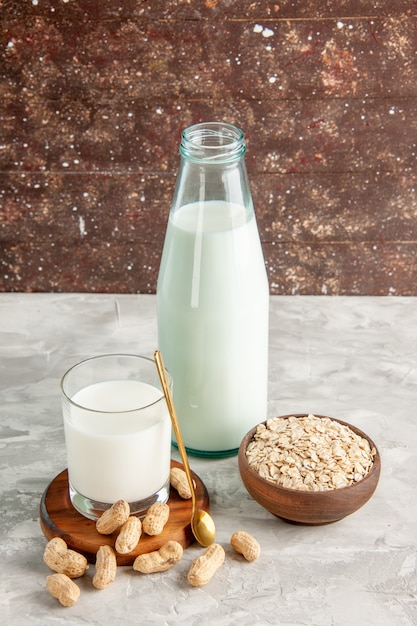 Bovenaanzicht van glazen fles en beker gevuld met melk op houten dienblad en droge vruchten lepel haver in bruine pot op witte tafel op bruine achtergrond