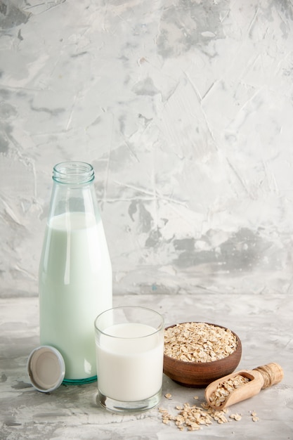 Bovenaanzicht van glazen fles en beker gevuld met melk op houten dienblad en gestapelde koekjes lepel haver in bruine pot op witte tafel op ijs achtergrond